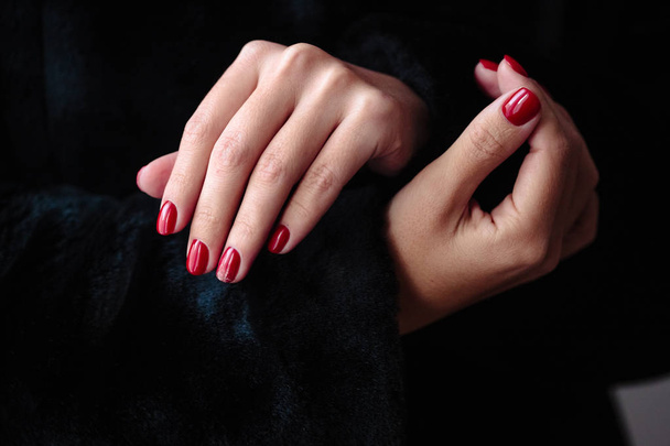 Gorgeous manicure, clssic red color nail polish, closeup photo. Female hands over dark fur background  - Fotoğraf, Görsel