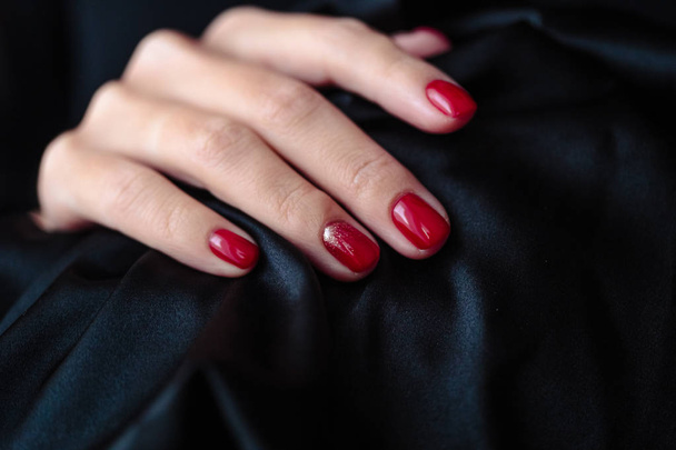 Gorgeous manicure, clssic red color nail polish, closeup photo. Female hands over dark fur background  - Foto, Bild