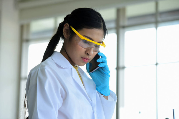 Naispuolinen tutkija työskentelee laboratoriossa ja puhuu matkapuhelimella
 - Valokuva, kuva