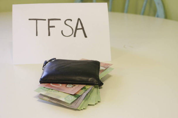 вывеска с надписью TFSA рядом с бумажником, в котором есть деньги. Тема канадских сбережений. TFSA расшифровывается как безналоговый сберегательный счет
 - Фото, изображение