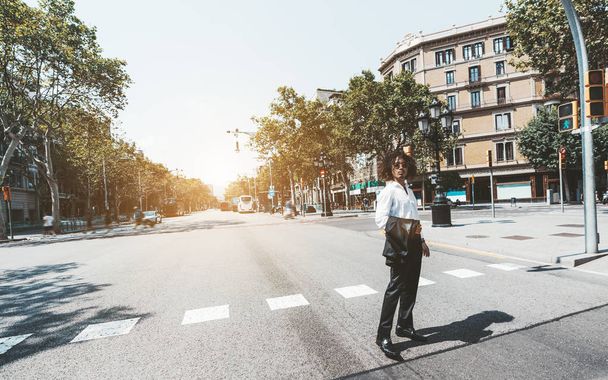 A young handsome businessman is crossing the street of a European city using pedestrian crossing; a curly Asian man entrepreneur is passing crosswalk, with a copy space place on the left for your text - Fotoğraf, Görsel