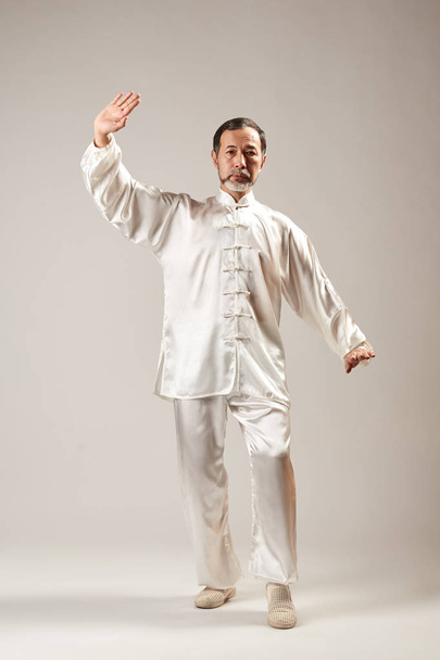 Senior master practicing qi qong taijiquan at studio. Breathing exercise and martial art moves, traditional chinese qi energy management gymnastics - Fotoğraf, Görsel