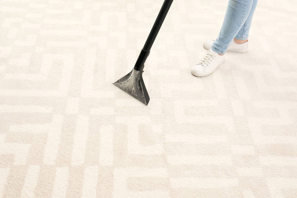 Woman removing dirt from carpet with vacuum cleaner indoors, closeup. Space for text - Фото, изображение