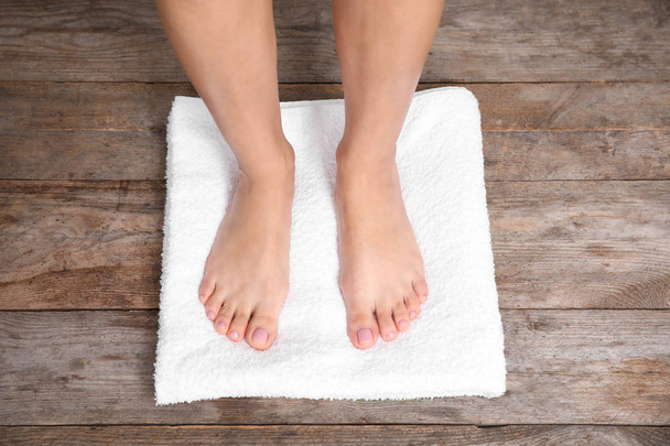 Woman with smooth feet and white towel standing on wooden floor, top view. Spa treatment - Foto, Imagen