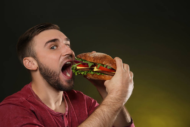 Young man eating tasty burger on color background. Space for text - Foto, immagini