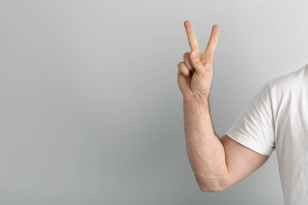 Young man showing victory gesture on light background. Space for text - Фото, зображення