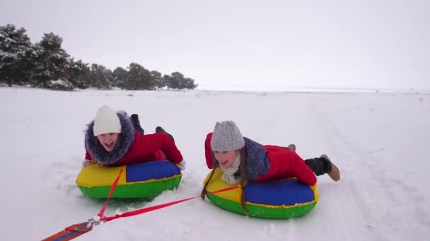 niños en chaquetas rojas en invierno paseo a través de la nieve en un tubo de nieve inflable y en trineo. deporte niñas relajarse en el parque de invierno para las vacaciones de Navidad. Movimiento lento
 - Metraje, vídeo
