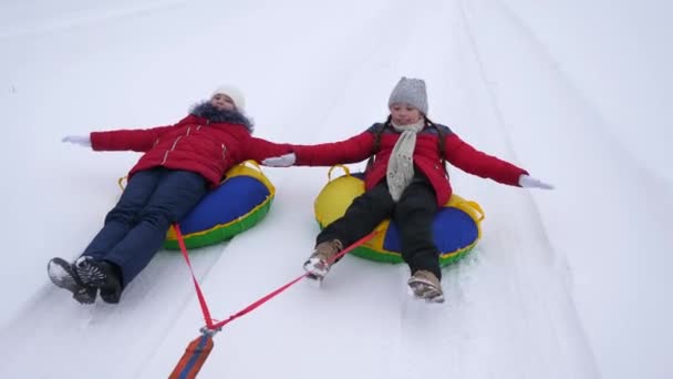 Ευτυχισμένος κορίτσια με έλκηθρο και ανάπαυσης στο χειμερινό πάρκο για τις διακοπές των Χριστουγέννων. τα παιδιά με κόκκινα σακάκια χειμώνα βόλτα στο χιόνι με έναν σωλήνα φουσκωτά χιόνι και παίξουν υπερήρωες. Αργή κίνηση - Πλάνα, βίντεο