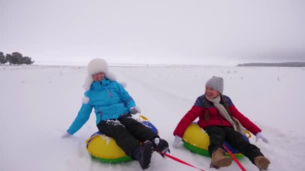 Happy mom and daughter sledding in winter in snow and playing snowballs. mother and child laugh and rejoice glide on an inflatable tube. Family playing park during the Christmas holidays. Slow motion - Footage, Video