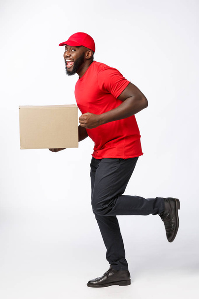 Retrato del repartidor afroamericano feliz en tela roja caminando para enviar un paquete de caja al cliente. Aislado en Grey studio Background. Copiar espacio
 - Foto, imagen