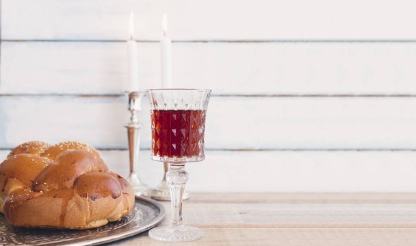 Shabbat or Sabbath kiddush ceremony composition with a traditional sweet fresh loaf of challah bread, glass of red kosher wine and candles on a vintage wood background with copy space - Photo, Image
