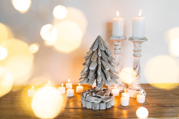White wooden Decorated Christmas Tree with Candles and Golden blurred shiny lights around. Place for Text. Hand Made Festive Concept - Zdjęcie, obraz