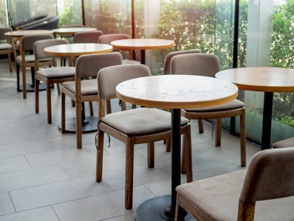 Okrągłe drewniane stoły i krzesła drewniane w pobliżu okna ze szkła w kawiarni z światło słoneczne. - Zdjęcie, obraz