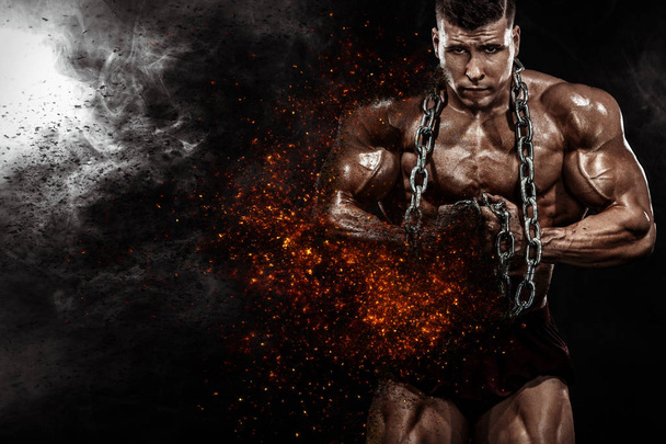 Brutal strong muscular bodybuilder athletic man pumping up muscles with chains on black background. Workout bodybuilding concept. Copy space for sport nutrition ads. - Fotó, kép
