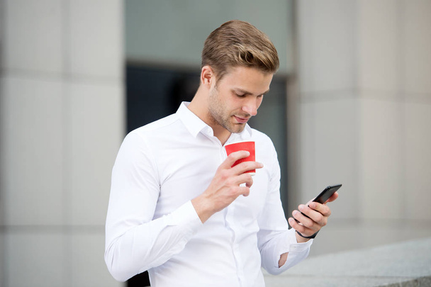 Send message. Man drinks coffee read message urban background. Start great day. Businessman relaxing with coffee morning time. Guy handsome attractive businessman need energy charge. Incoming message - Foto, imagen