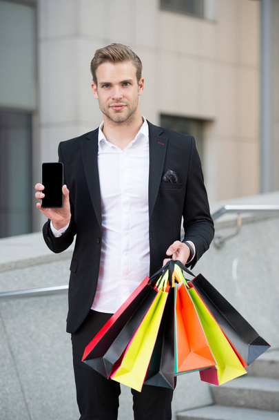 Shopping online. Businessman use shopping application. Man carries shopping bags while hold phone urban background. Successful businessman shopping online. Busy people appreciate online service - 写真・画像