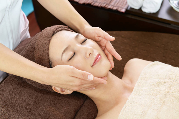 krásná mladá žena přijímá masáž obličeje se zavřenýma očima ve spa salonu  - Fotografie, Obrázek