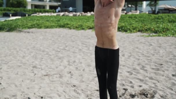 Slow motion steadicam shot, atlético hombre sin camisa haciendo ejercicios de estiramiento en la playa de arena
. - Metraje, vídeo