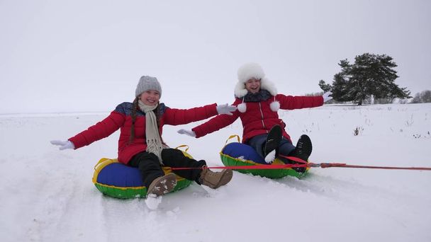 діти слайди в снігу на надувних сніг трубки і хвилі руку. Щасливих дівчаток слайди по снігу на санях. діти грають у парку на різдвяні свята, взимку - Фото, зображення