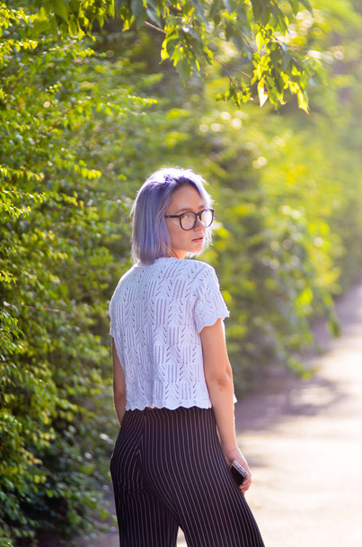 Pouliční móda. Stylový vzhled. Bokové modré vlasy dívka v brýlích pózuje před kamerou v parku. - Fotografie, Obrázek
