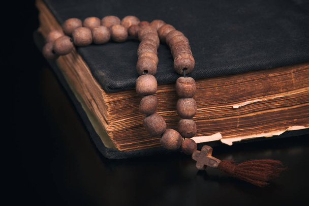 Old book and church rosary on a black background - Fotoğraf, Görsel