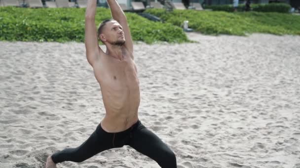 Slow motion steadicam shot, athletic shirtless man doing stretching exercises on sandy beach. - Video