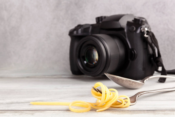 Spaghetti su forchetta e macchina fotografica dslr su tavolo in legno. Concetto di fotografia alimentare
.  - Foto, immagini