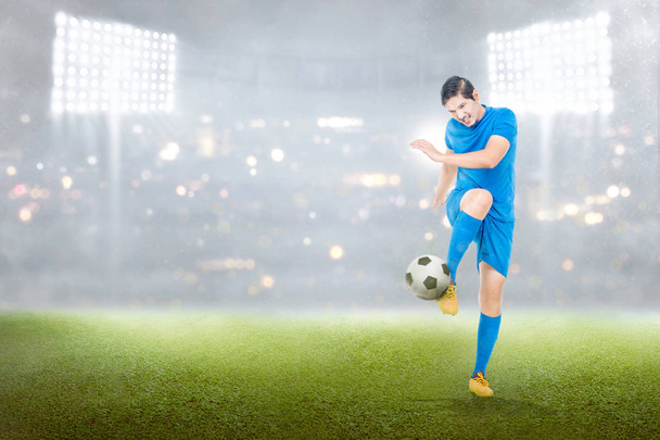 Handsome asian soccer player man in action with ball on stadium field - Photo, image
