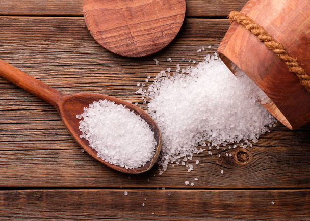 Salt scattered on a wooden table. A barrel and a spoon with salt. - Фото, изображение