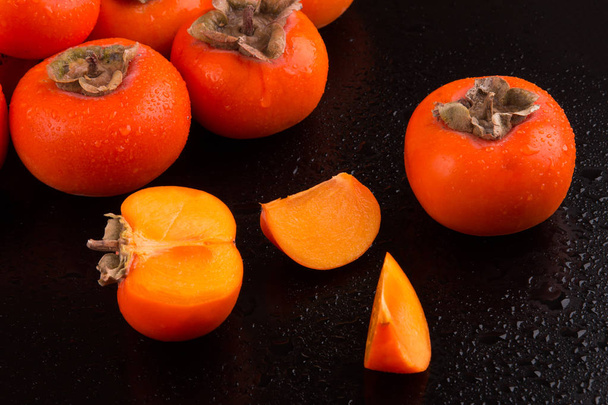 Fruits of juicy persimmons on a black background - Zdjęcie, obraz