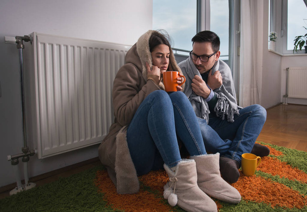 Giovane coppia in giacca e coperto con coperta seduta sul pavimento accanto al radiatore e cercando di riscaldarsi
 - Foto, immagini