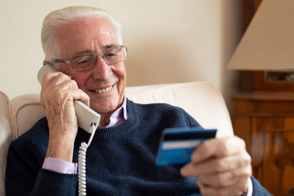 Senior Man At Home Giving Credit Card Details On The Phone - Foto, imagen