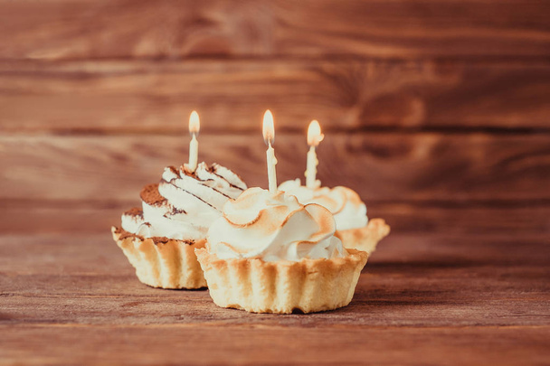 Three holiday birthday cupcakes with burning candles on a wooden background. - Foto, immagini