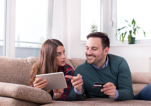 Młoda para z tabletu i karty kredytowej zakupów online z sofą w domu - Zdjęcie, obraz