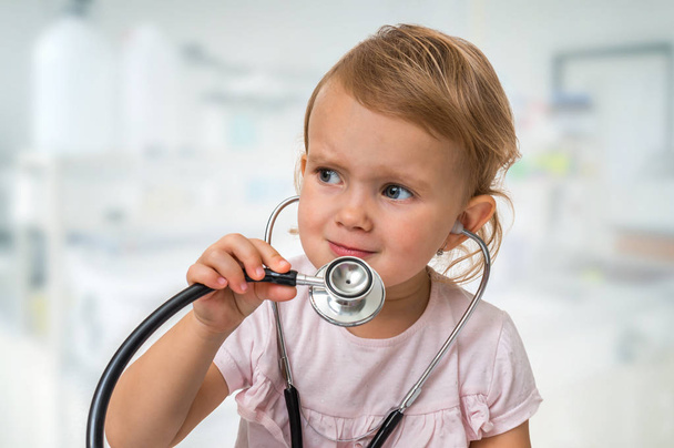 Little baby plays doctor with stethoscope in hands - Φωτογραφία, εικόνα