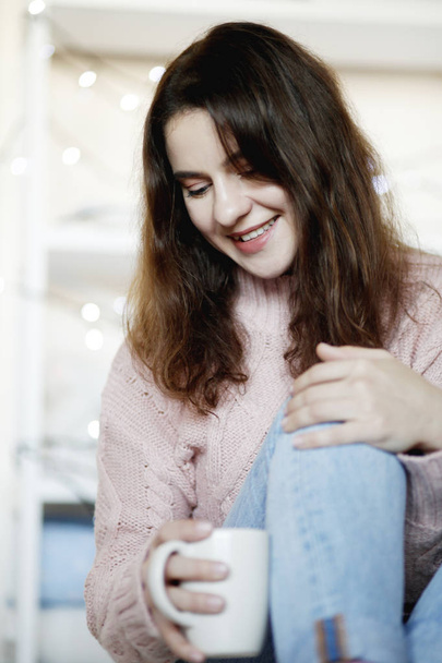 Closeup portrait of beauty brunette woman wearing blue jeans and winter sweater holding cup of hot tea, blurred background - Fotografie, Obrázek