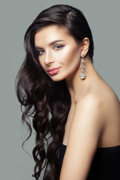 Attractive woman with long curly hair, makeup and diamond jewelry earrings - Fotoğraf, Görsel