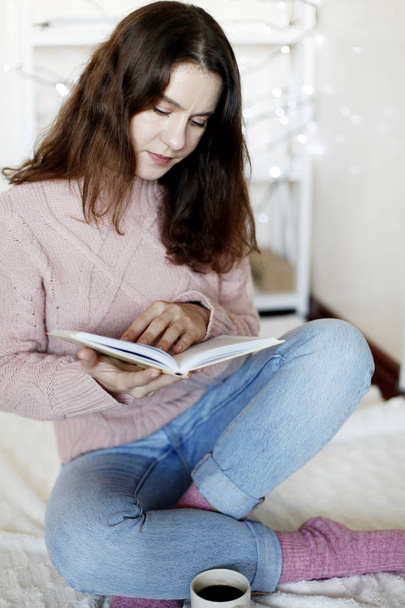 Closeup retrato de beleza morena mulher vestindo jeans azul e camisola de inverno leitura livro em casa, fundo borrado
 - Foto, Imagem