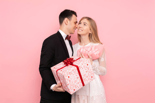 A loving couple, a man gives a woman a bouquet of tulips and a box with a gift on a pink background. Valentine's Day - Foto, afbeelding