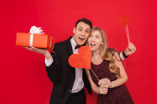 Portrait of a happy couple, man holding paper hearts, on red background, lovers day - Fotó, kép