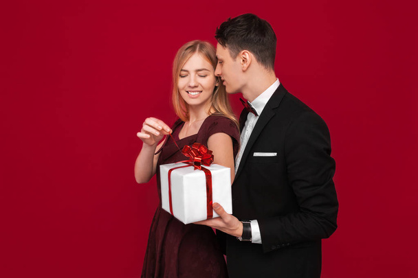 An elegant man in a suit gives a surprise to a woman, gives her a gift, on a red background - 写真・画像