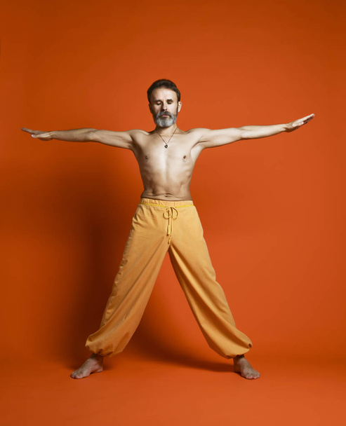 オレンジ色の背景に分離運動ヨーガ アーサナ足を行うフィットネス年配の男性 - 写真・画像