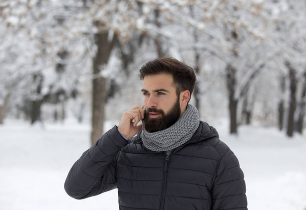 Bello giovanotto con la barba che parla al cellulare nella foresta con la neve
 - Foto, immagini