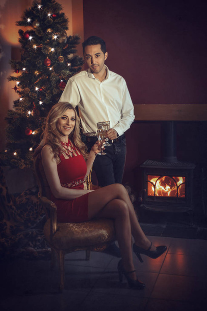 Loving couple in front of a roaring log fire celebrating Christmas with champagne - Фото, изображение