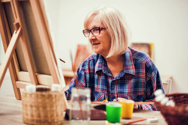 Idős asszony festészet otthonában. Nyugdíj-hobbi.  - Fotó, kép