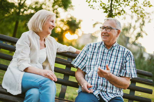 Zwei glückliche Senioren sitzen im Park und unterhalten sich.  - Foto, Bild