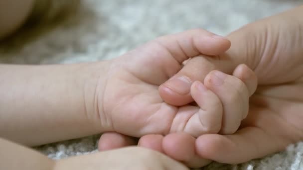 Mamá está cogida de la mano del pequeño bebé. Cuidado materno de niños pequeños. Primer plano
 - Metraje, vídeo