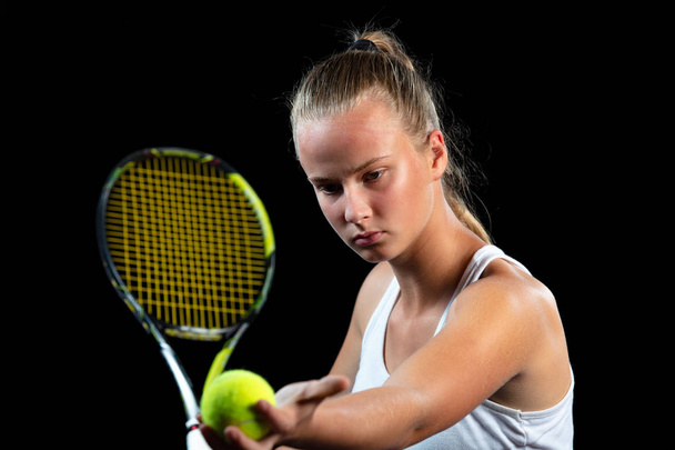 Young woman on a tennis practice. Beginner player holding a racket, learning basic skills. Portrait on black background. - Foto, Imagem