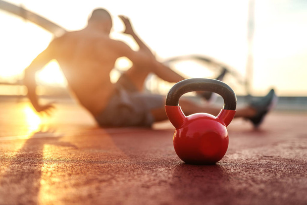 Silhouette of shirtless man doing crunches in the court in the morning. Selective focus on kettlebell. - Photo, Image