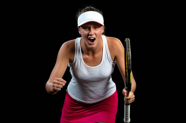 Beautiful girl tennis player with a racket on dark background wiht lights celebrating flawless victory - 写真・画像